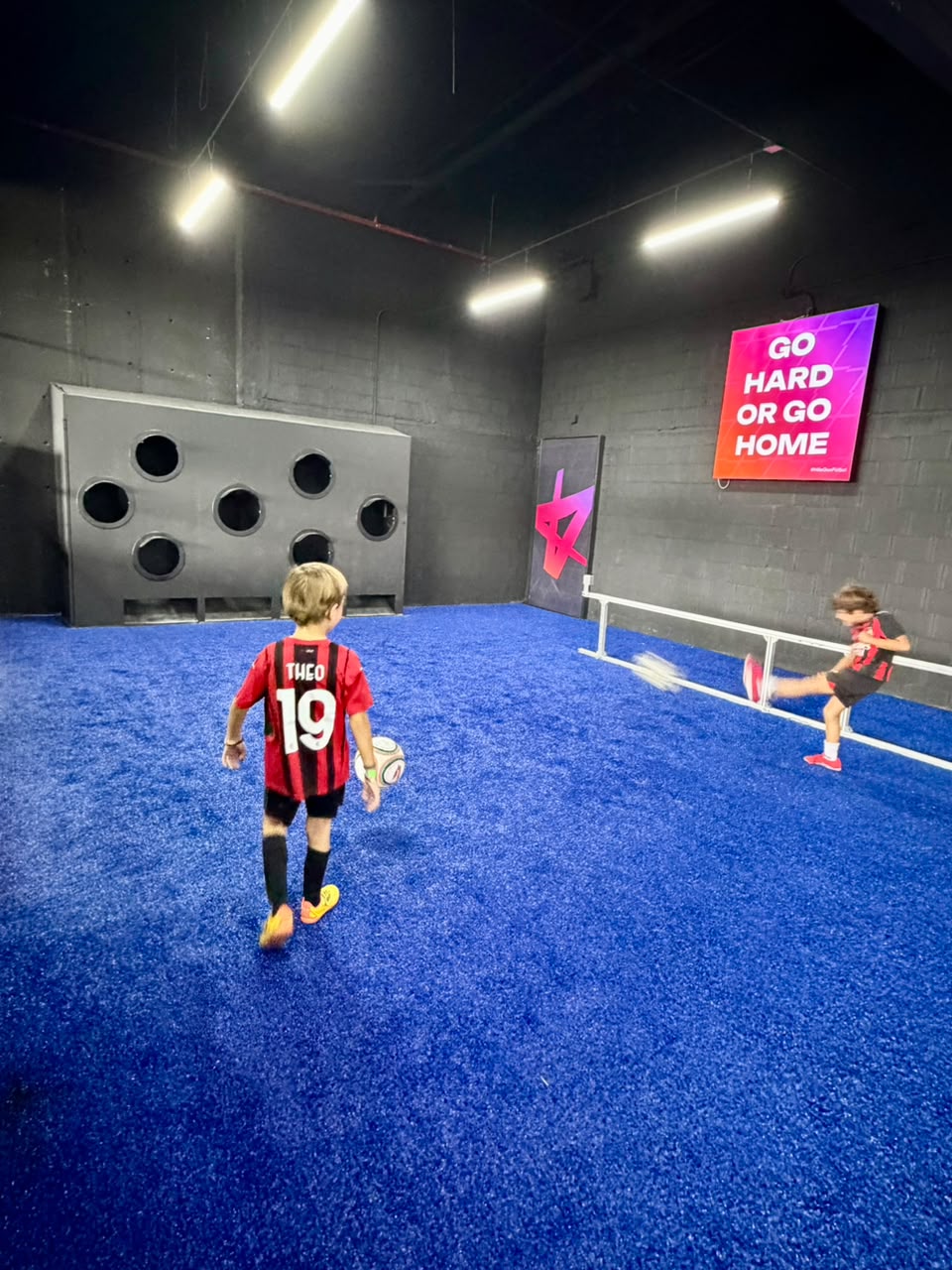 Niños jugando frente al muro de objetivos y una red baja en Kick Zone