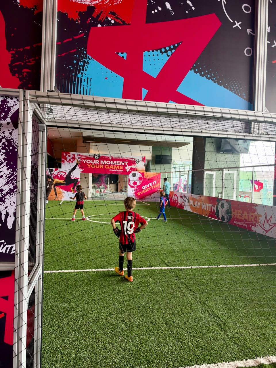 Niños jugando fútbol en la cancha de Kick Zone, rodeados de murales y redes